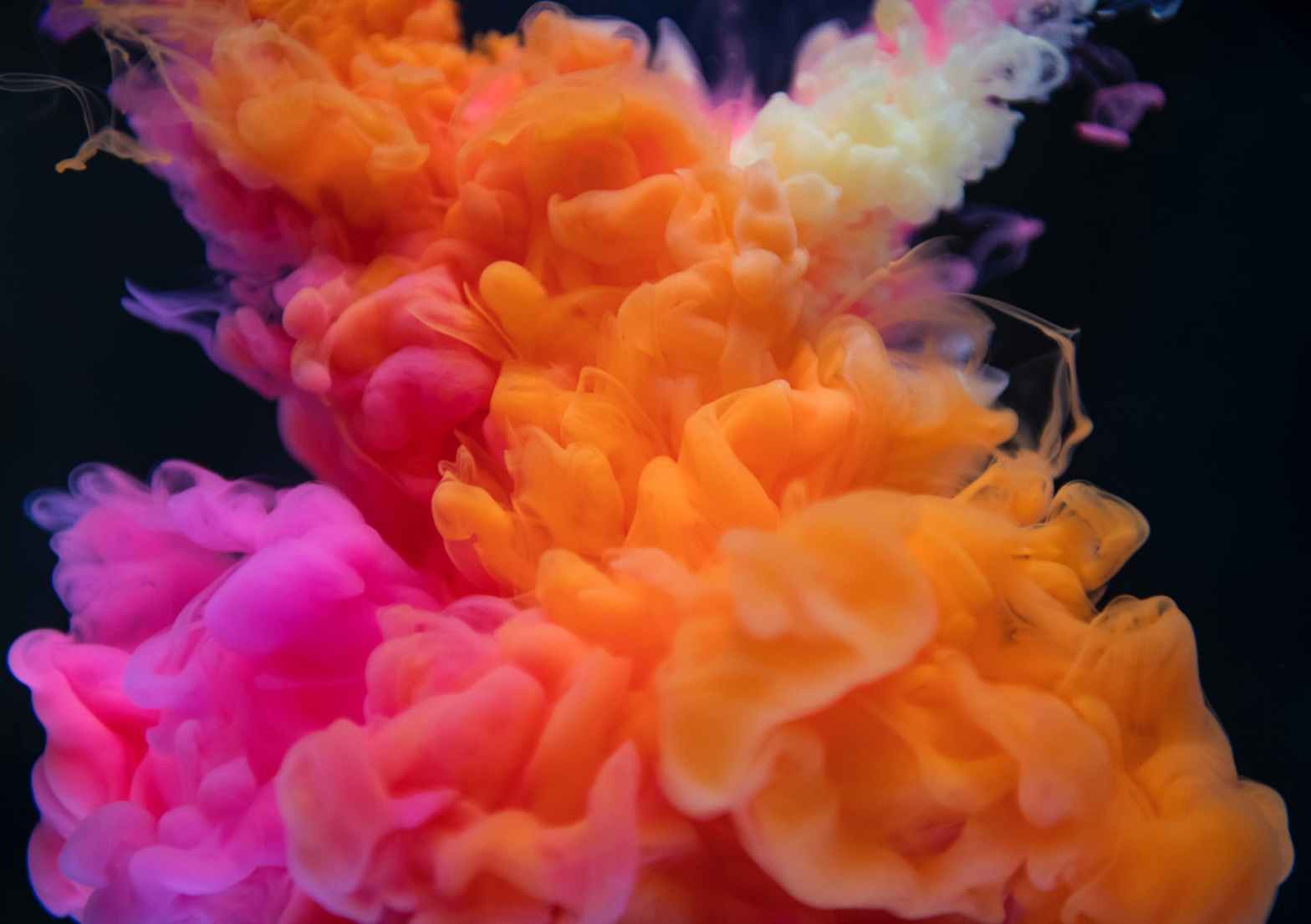 Pink, orange and pale yellow coloured smoke swirl into one another in front of a black background.